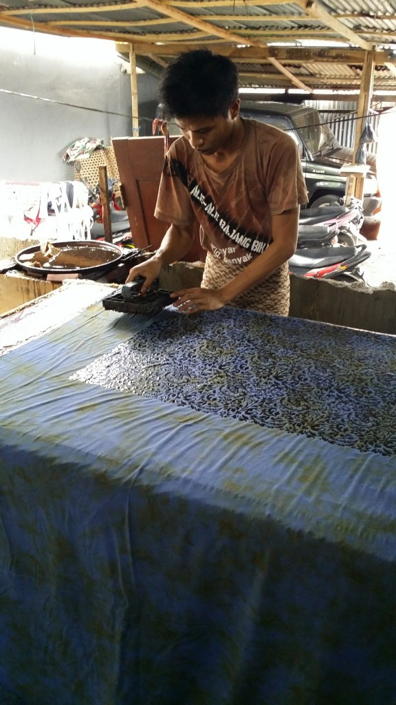 Batik Fabric uses a wax resist process, here the batik maker is applying the was using a copper stamp.
